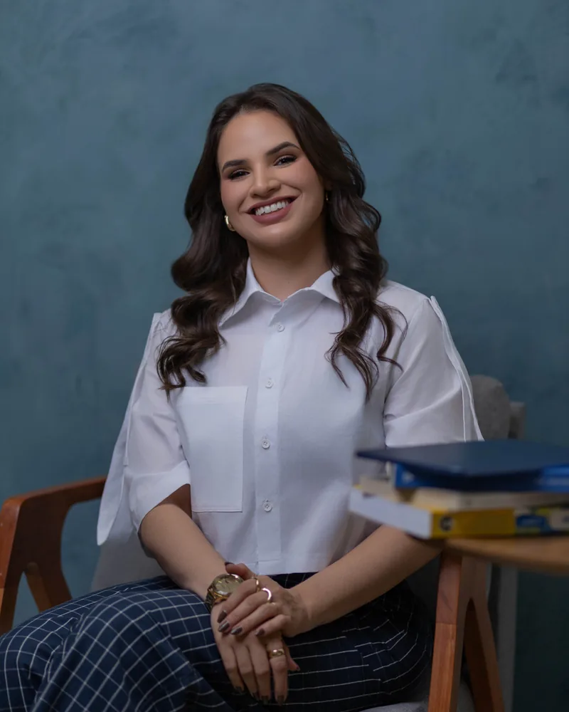Dra. Hanna Beatriz sentada ao lado de uma mesa com livros de medicina